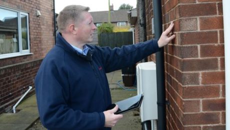 A surveyor checking external brickwork of house holding a tablet