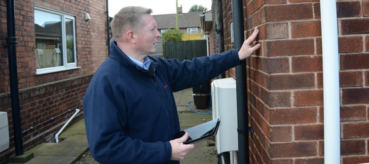 A surveyor checking external brickwork of house holding a tablet
