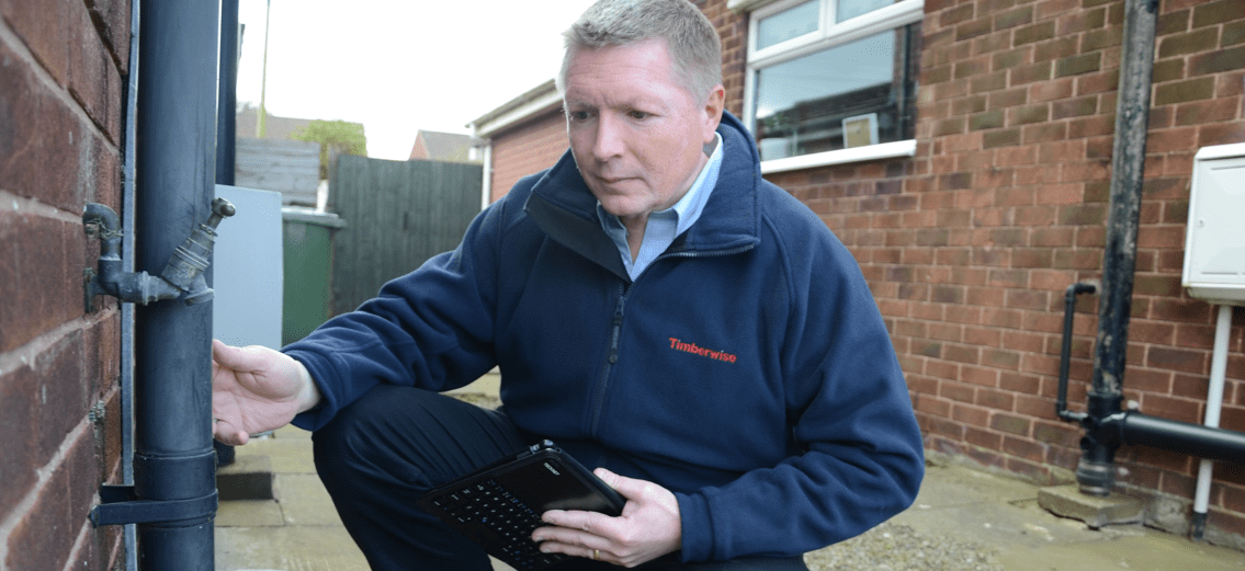 Man inspecting a drainpipe outside a house