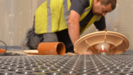 Man on his knees looking at a basement sump and pump