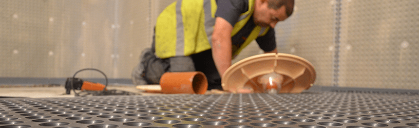 Man on his knees looking at a basement sump and pump