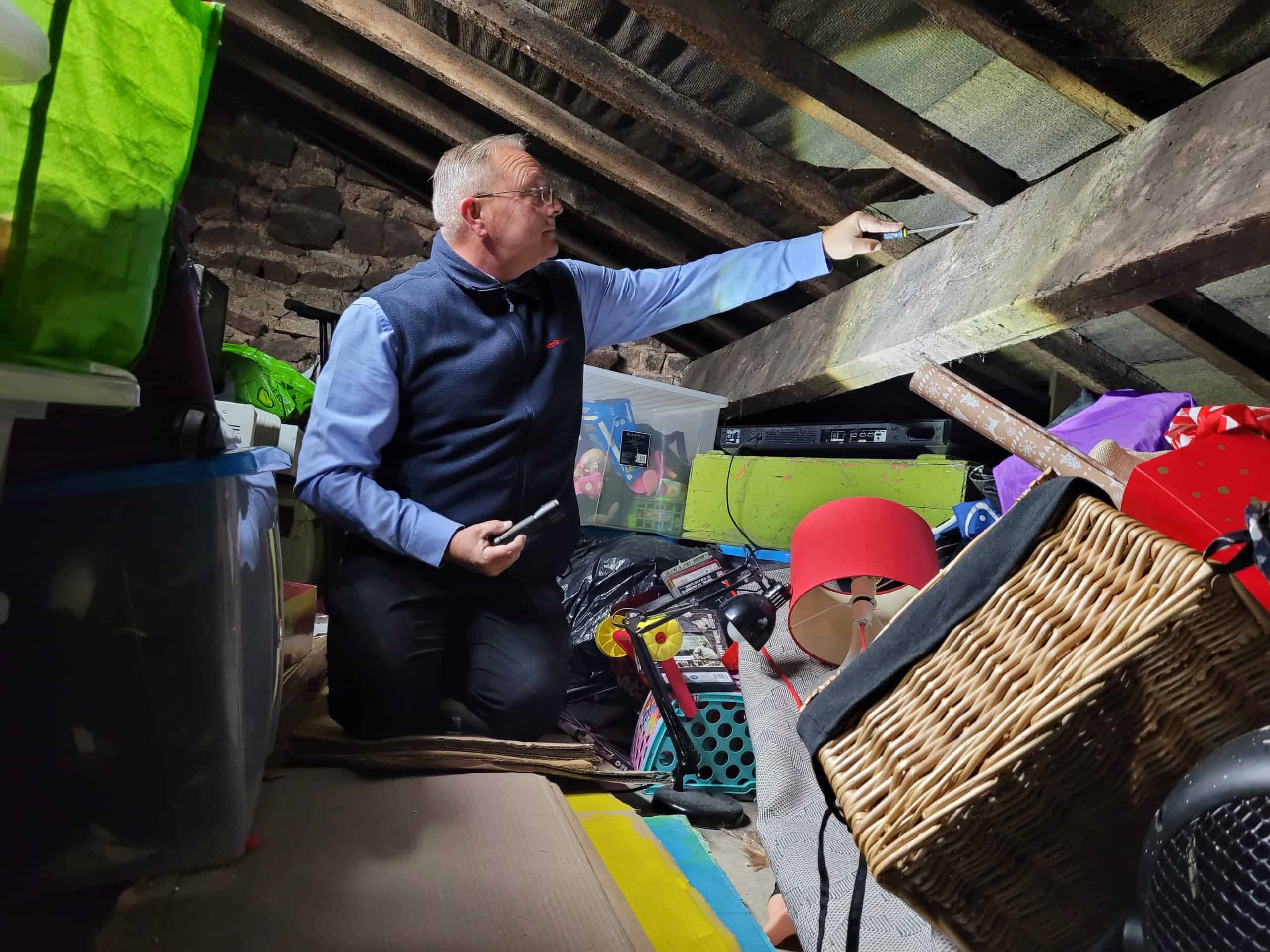 Male Timberwise surveyor kneeling in a loft checking the condition of the roof timbers with a screwdriver