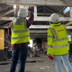 2 surveyors in full PPE looking and pointing up to the roof