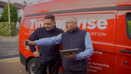 Male Timberwise technician and male surveyor stood with a tablet and pointing next to a red branded van