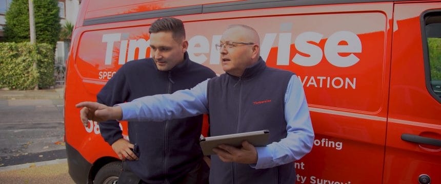 Male Timberwise technician and male surveyor stood with a tablet and pointing next to a red branded van