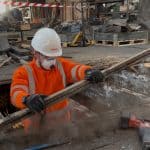 Construction technician worker in full PPE removing wet rot affected floorboards