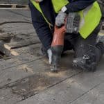 Construction technician worker in full PPE using a hand electric tool to cut through floorboards