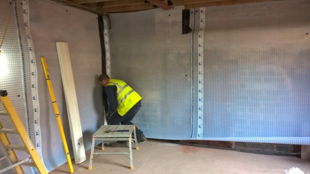 A man fitting cavity drain membrane in a basement