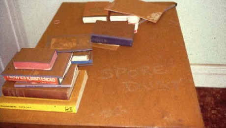 A chest of draws with a collection of books on top covered in dry rot spore dust